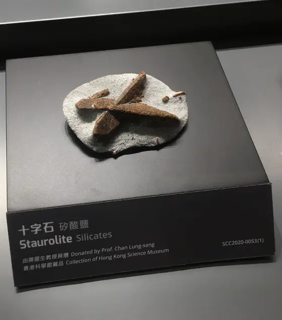 Reddish-brown cross-shaped twinned staurolite specimen displayed on a pale base